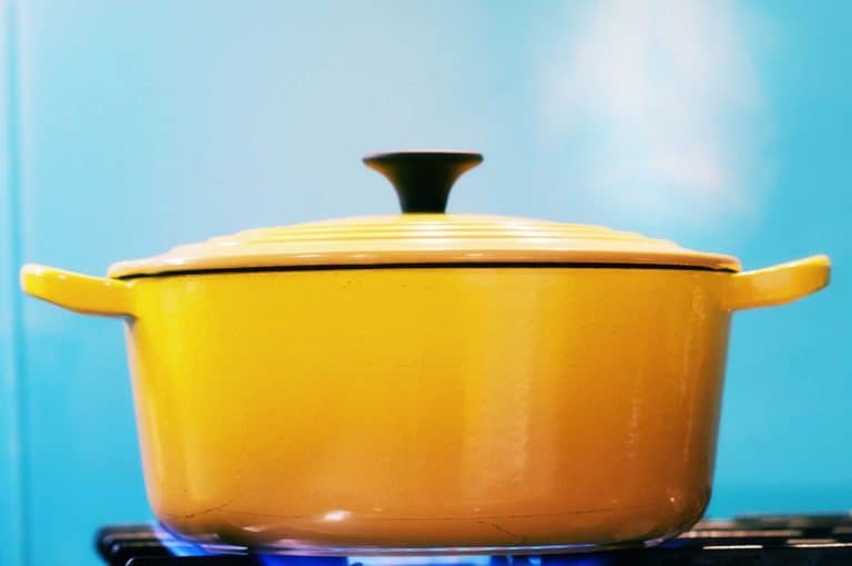 A yellow enamel casserole pots, with its lid on, sits on a lit gas burner creating steam as it heats, Are Enamel Pots Oven Safe?