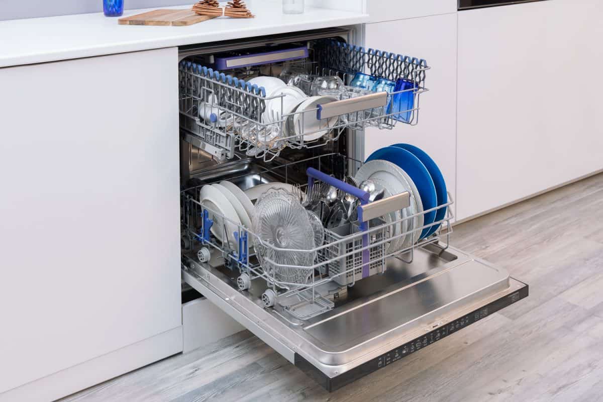 An open dishwasher with plates, spoons and other utensils