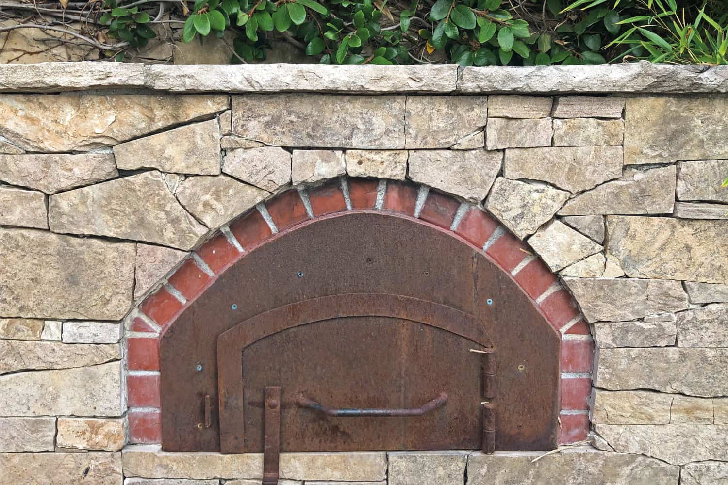 An outdoor, pizza oven with metal door, brink, and stone.