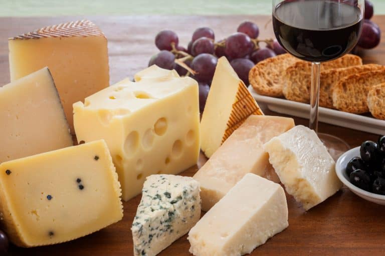 Assorted cheeses (such as ementhal, blue cheese, pecorino, parmesan and manchego among others) served with bread, grapes, black olives and a glass of red wine on a wooden table, Should Cheese Be Served At Room Temperature?