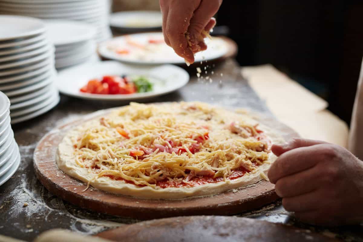 Chef sprinkling grated cheese on pizza top