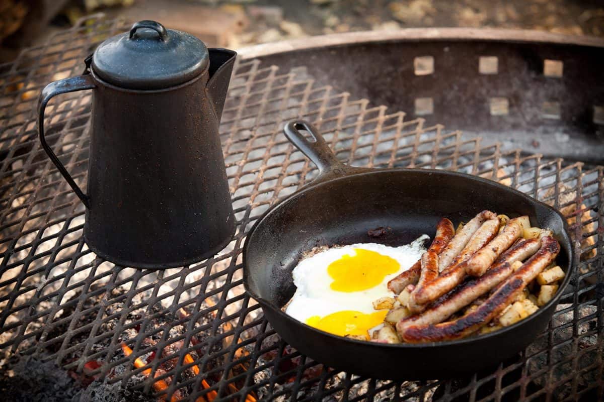 Cooking breakfast eggs and sausage over a campfire with coffee