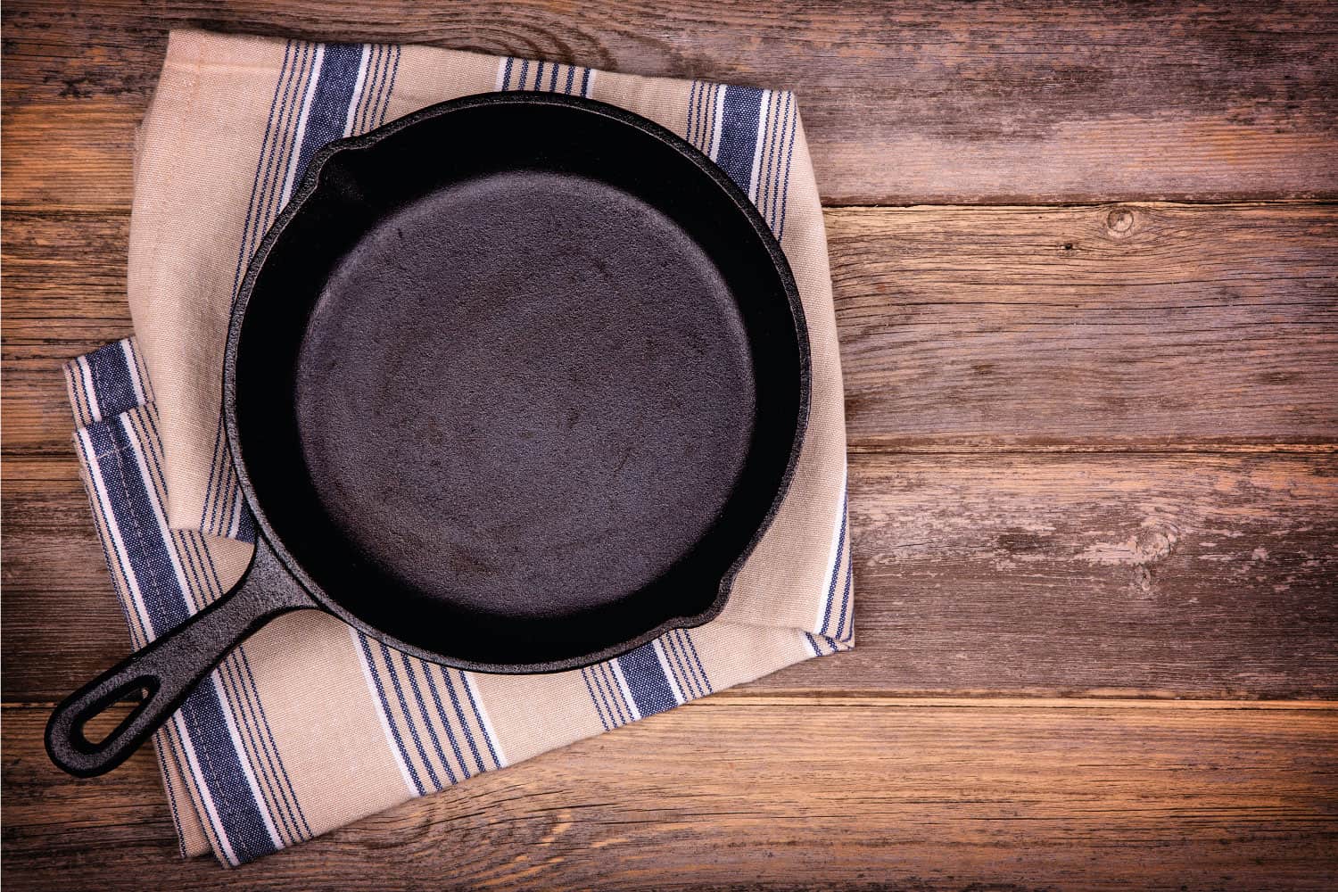 Empty cast iron skillet with tea towel, over old wood background