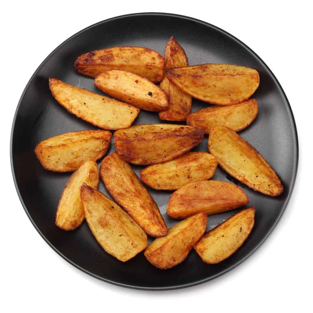 Fried potato wedges inside a small black plate on a white background