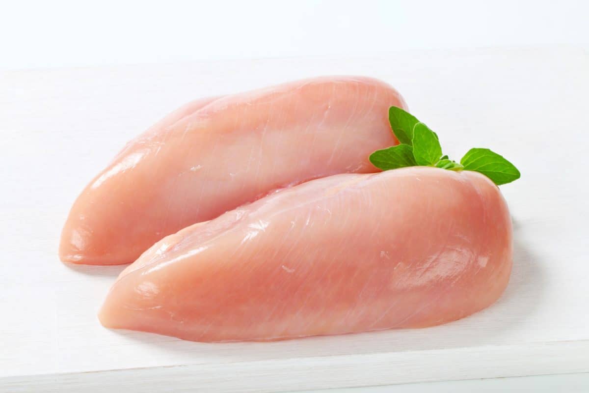 Glistening chicken breast with basil on top on a white background