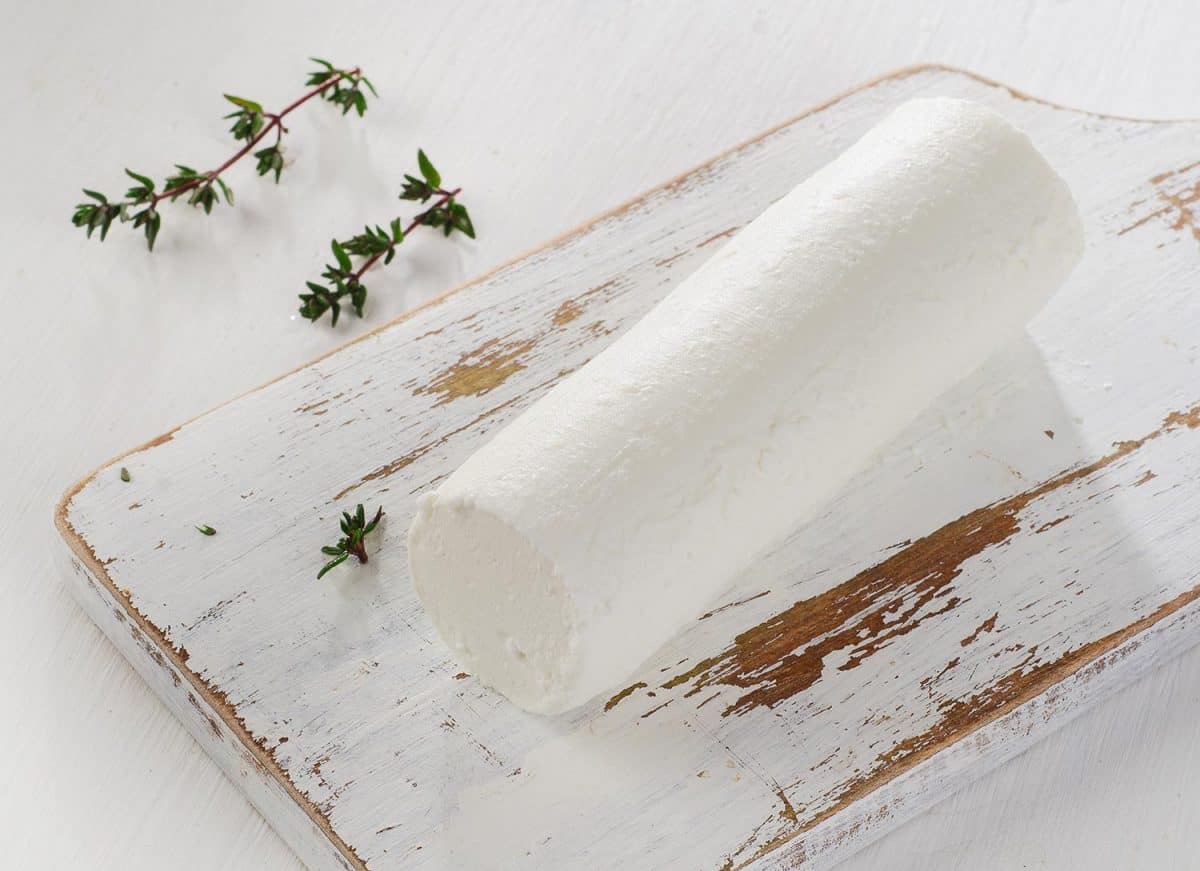 Goat cheese with fresh herbs on white wooden table