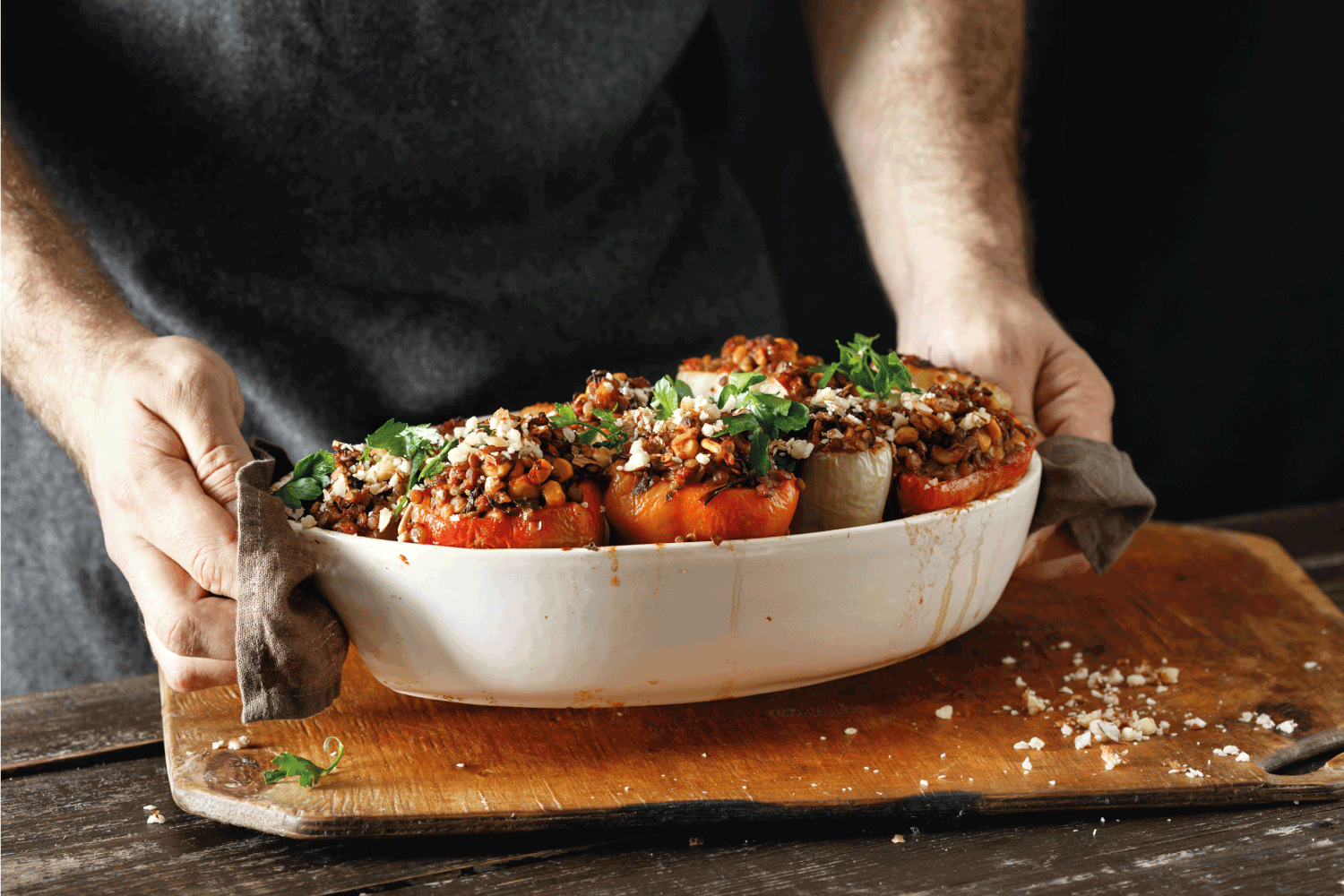 Male hands holding cooked stuffed peppers with green lentils, corn, salsa and almonds in baking dish on wooden table