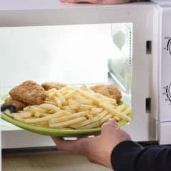 Person putting fried food inside microwave oven, How To Properly Warm Up French Fries [In Multiple Appliances!]
