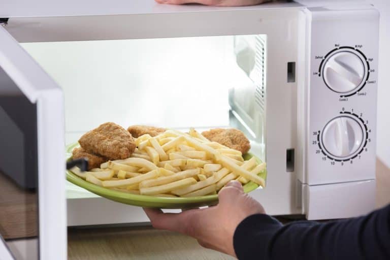 Person putting fried food inside microwave oven, How To Properly Warm Up French Fries [In Multiple Appliances!]