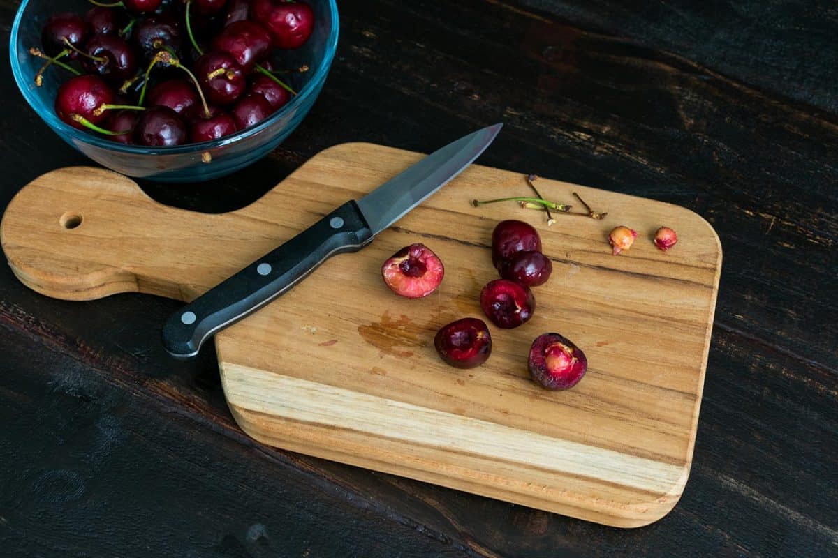 Stemming and pitting fresh bing cherries with a paring knife on a wood cutting board
