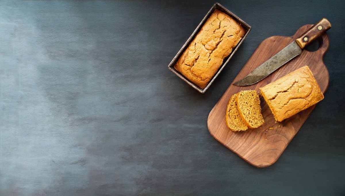 Two freshly baked homemade pumpkin bread loaves with knife over dark background. Image shot from top view, flatlay.