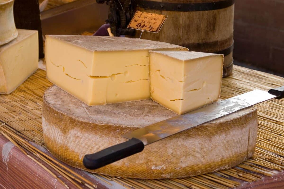 Wheel of cut gruyere cheese on a table with a knife