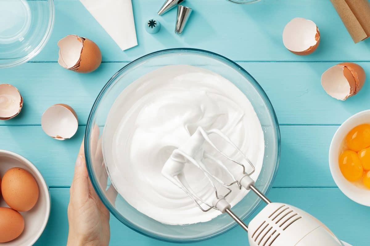 Whipped egg whites cream to perfect peaks in glass bowl with mixer and hand on blue wooden table. Step by step recipe of meringue cookies top view, How To Store Meringue Overnight