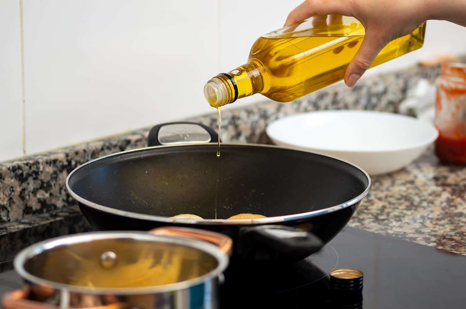 Woman pouring cooking oil from bottle into frying pan