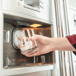 Woman's hand holds glass and uses refrigerator to make fresh clean ice cubes. How Long To Defrost Samsung Ice Maker