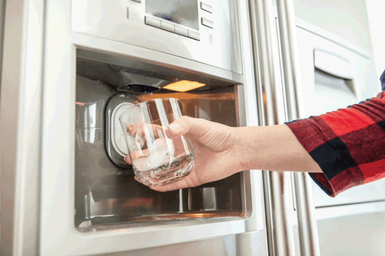 Woman's hand holds glass and uses refrigerator to make fresh clean ice cubes. How Long To Defrost Samsung Ice Maker