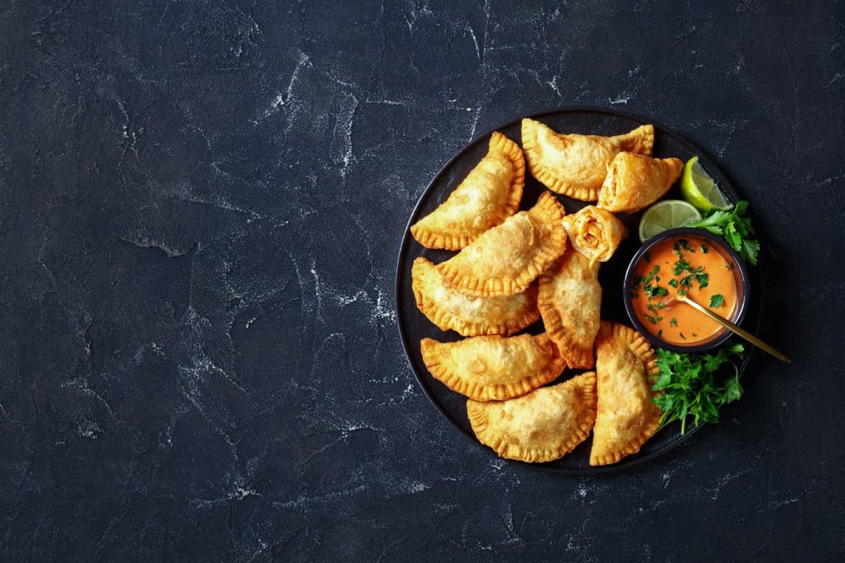 delicious deep fried Buffalo Chicken Empanadas with Low Calorie Dip on a black platter on a concrete table