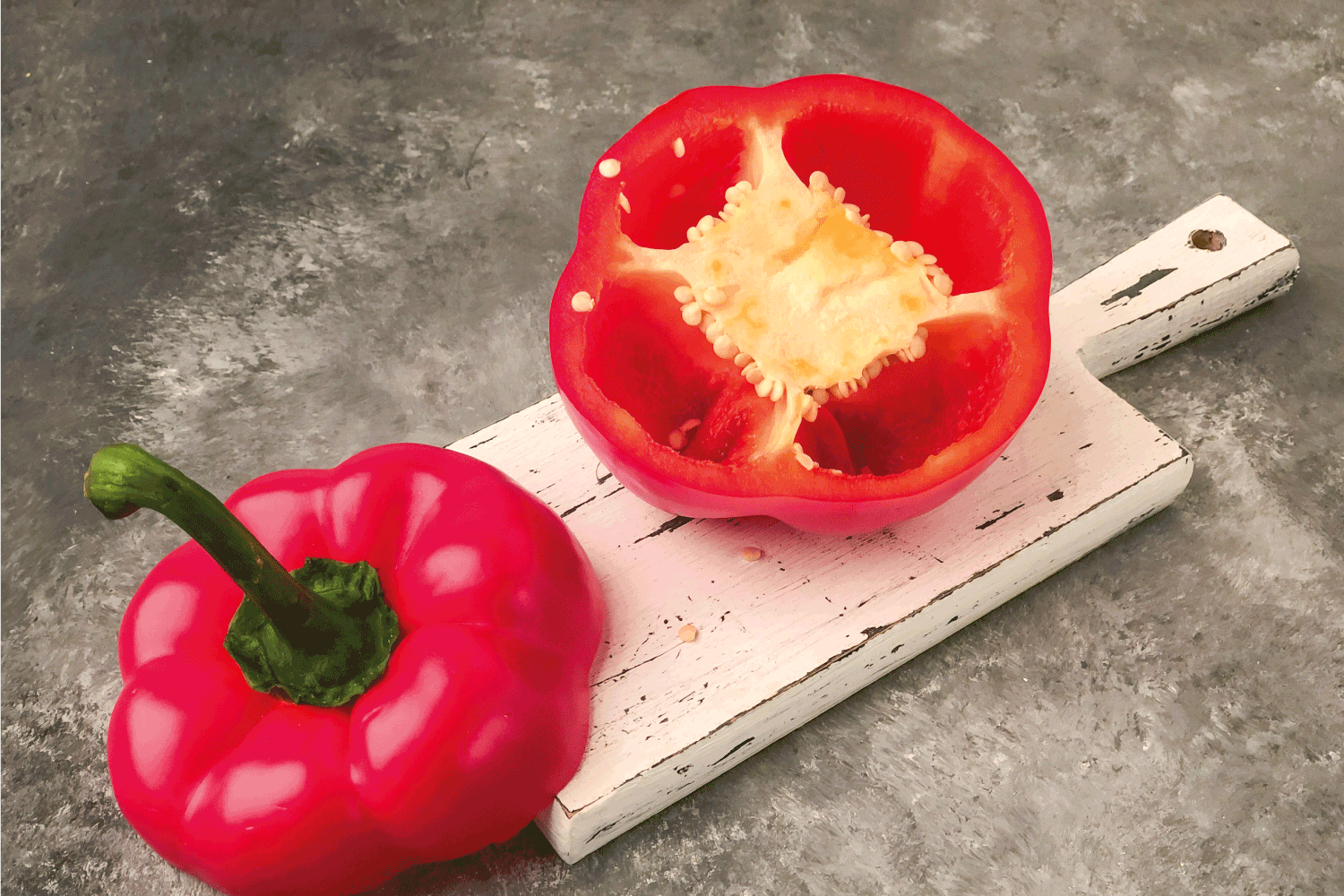 halved red bell pepper on a wooden cutting board on gray background