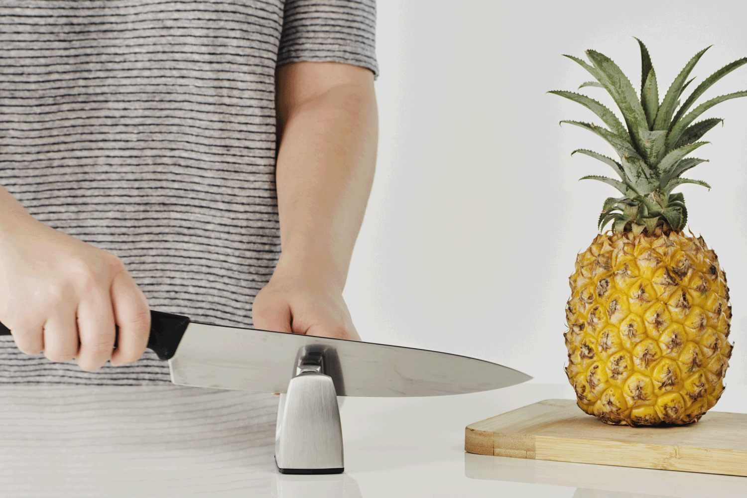 woman sharpening a knife before cutting into a pineapple in the kitchen