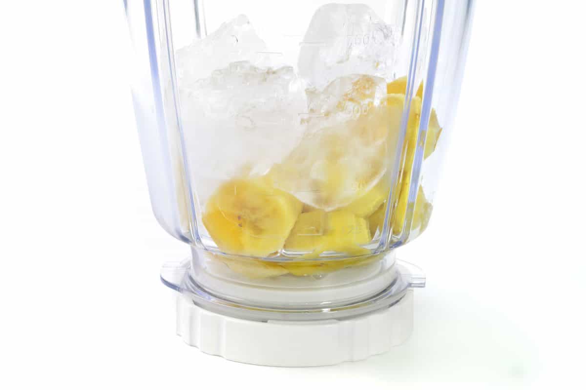 A blender with ice and banana on a white background