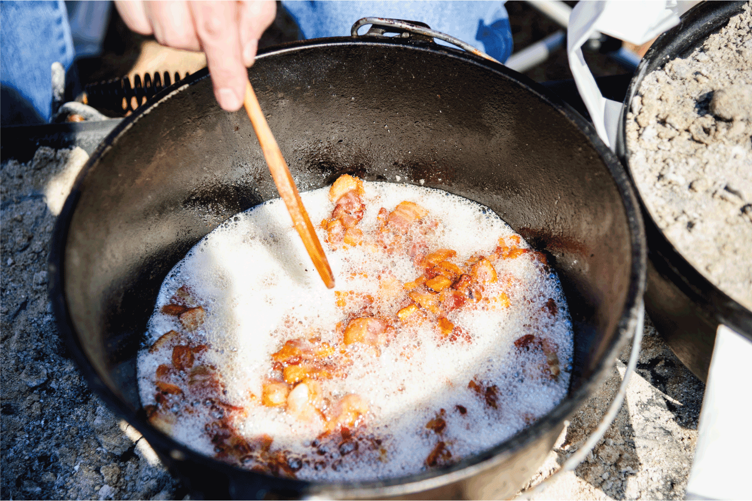 A dutch oven containing bacon frying in its grease.