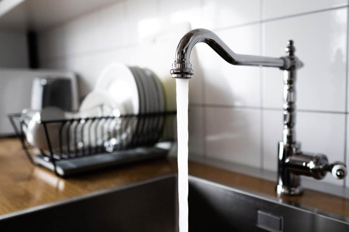A faucet left open in the kitchen sink with newly washed dishes on the dishrack