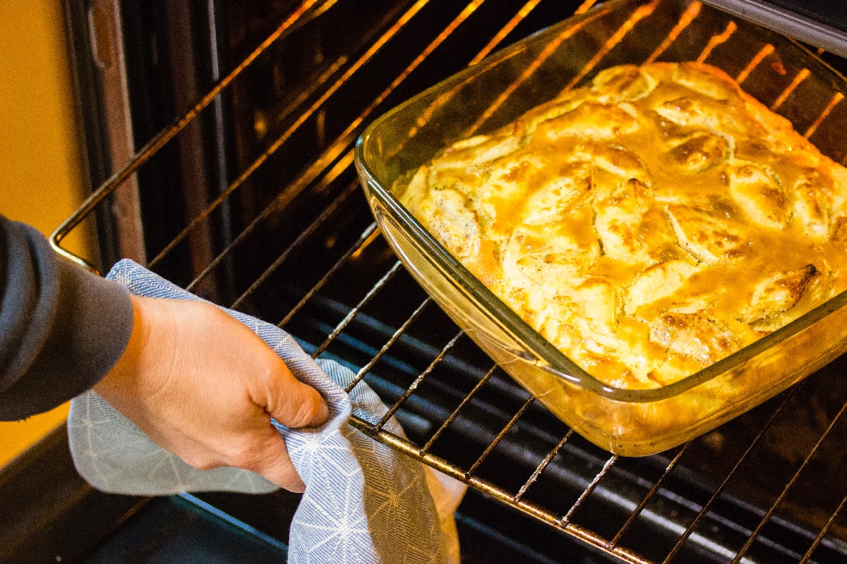 A woman's hand pulls a glass container with a traditional American apple pie from the oven
