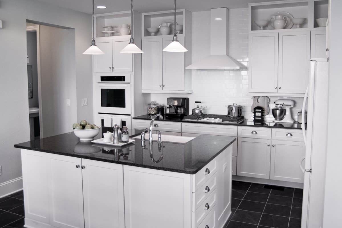 Contemporary kitchen incorporated with white tires, white cabinetry and black floor tiles