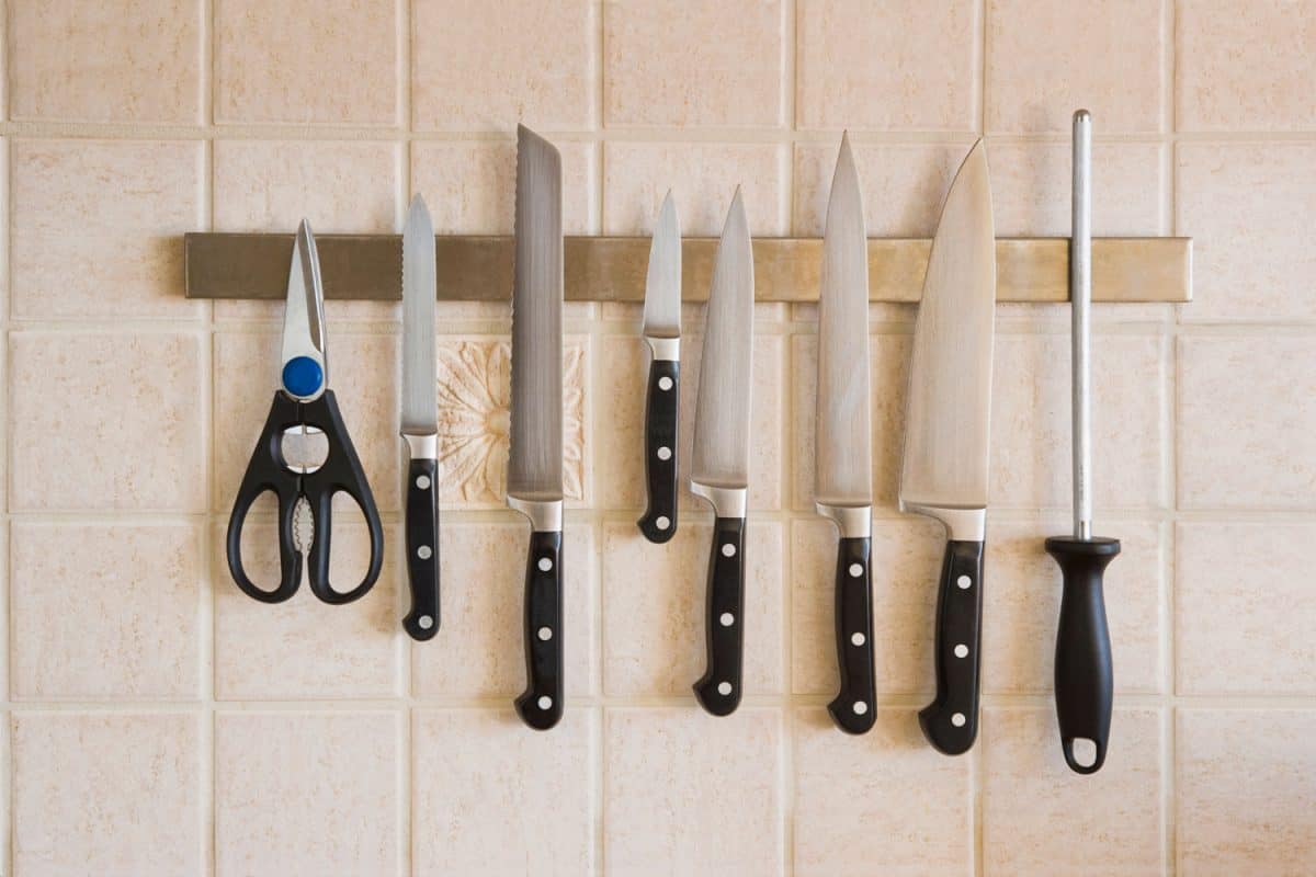 Different kitchen knives and scissors hanged on the kitchen wall