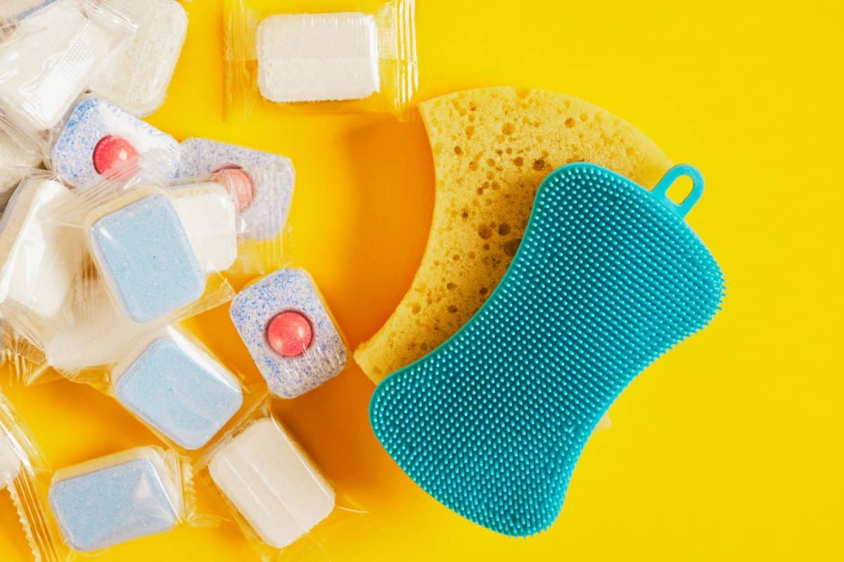 Dishwasher tablets and scrubbing spongers on the side on a yellow background