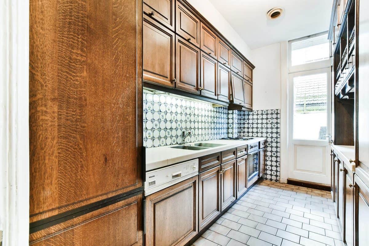 Retro style home interior design of narrow kitchen with wooden cupboards and ceramic tile walls