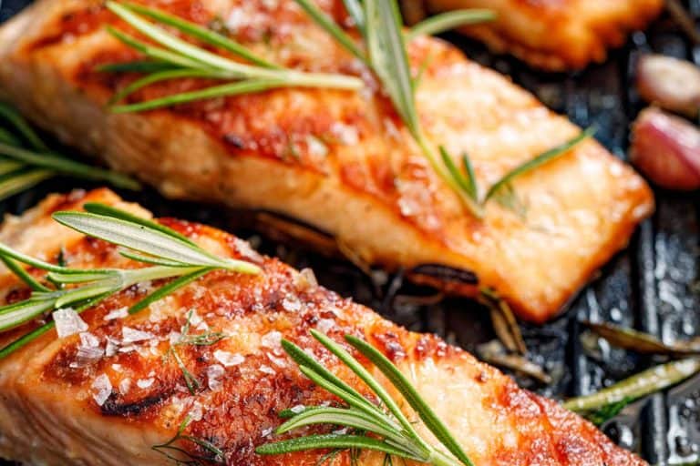 Salmon fillets sprinkled with fresh herbs and lemon juice on a grill plate, Should You Fry Or Bake Salmon?