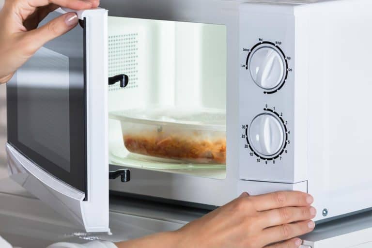 Woman closing microwave door, Are Glass Containers Oven Safe? [Here's How To Tell]