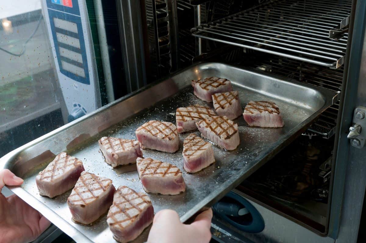 close up on chef putting plate with char-grilled tuna steaks into the oven