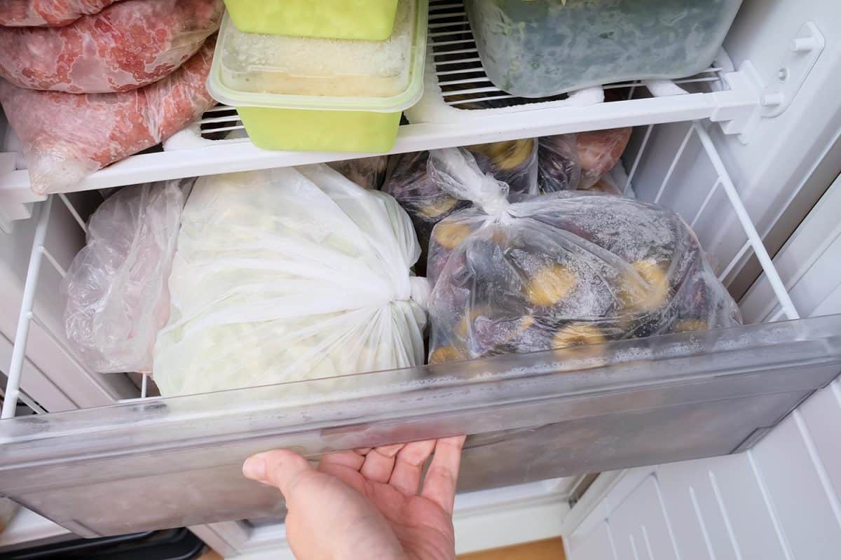 A hand opening a drawer of a freezer with frozen foods