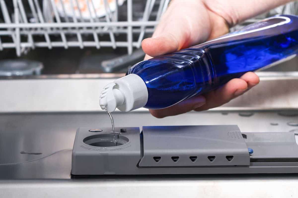 A man pours a rinse aid into the dishwasher compartment