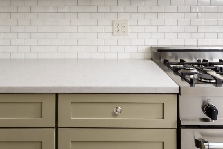 A photo of a white kitchen countertop, light gray kitchen cabinets and a socket on the backsplash, How High Should Kitchen Counter Outlets And Light Switches Be?