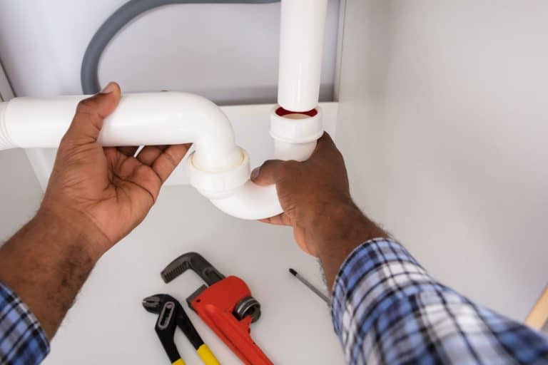 A plumber installing a P-trap under the sink, Does A Garbage Disposal Need A P-Trap?