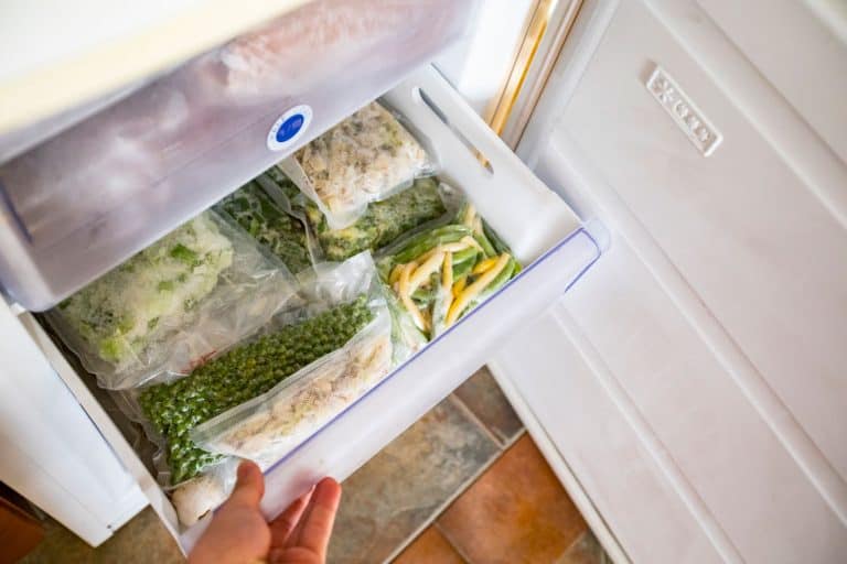 A woman checking the freezer drawer filled with vegetables, How To Repair A Cracked Freezer Drawer
