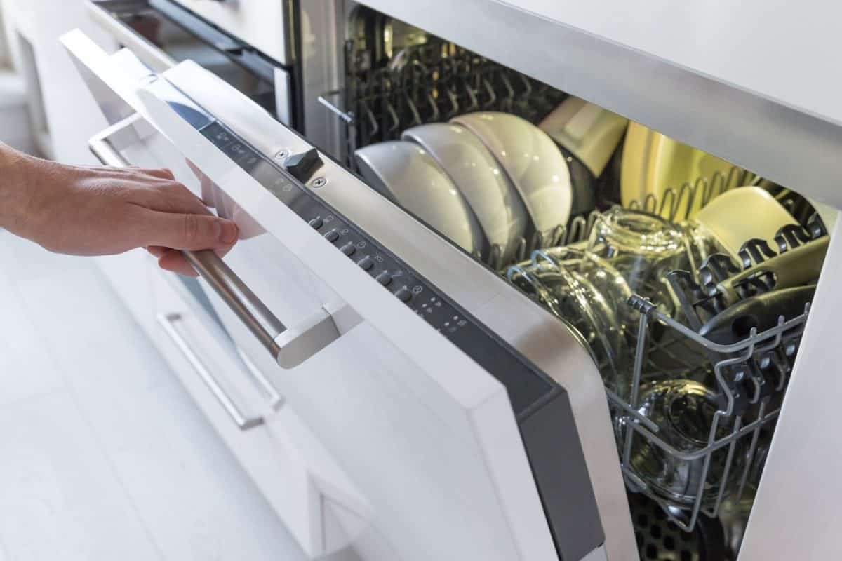 A woman opening the dishwasher containing dishes and kitchen utensils