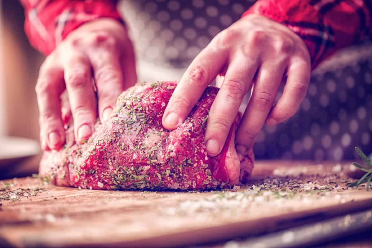 A woman rolling a big slice of steak on salt and other spices
