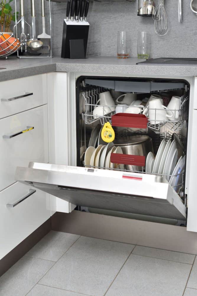An opened dishwasher with lots of kitchen utensils under kitchen sink