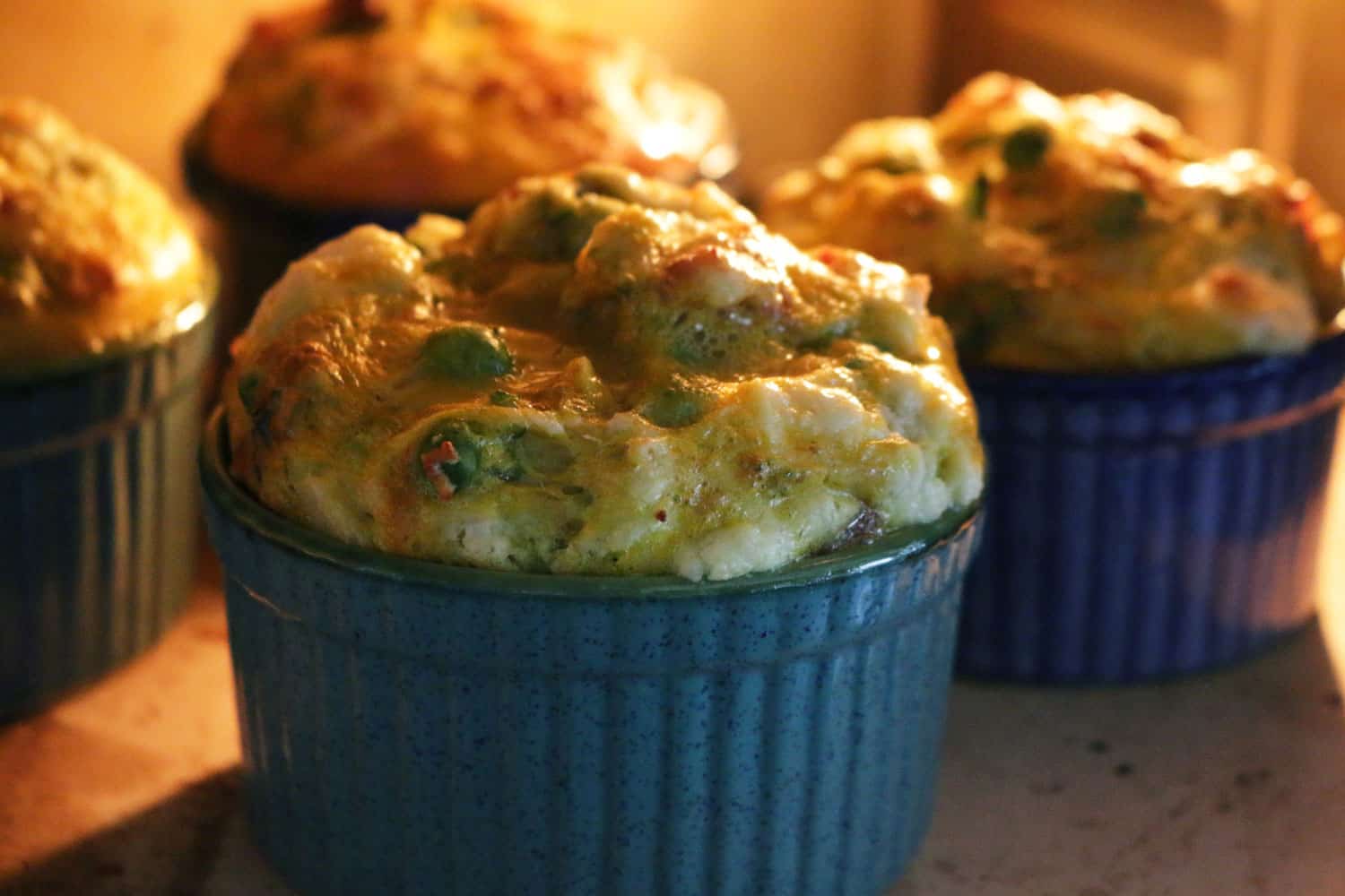Close-up image of homemade egg and spinach breakfast muffins served in blue ramekin dishes in hot oven, home baking