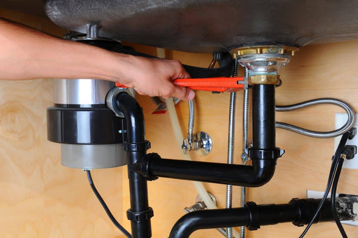 Closeup of a plumber using a wrench to tighten a fitting beneath a kitchen sink