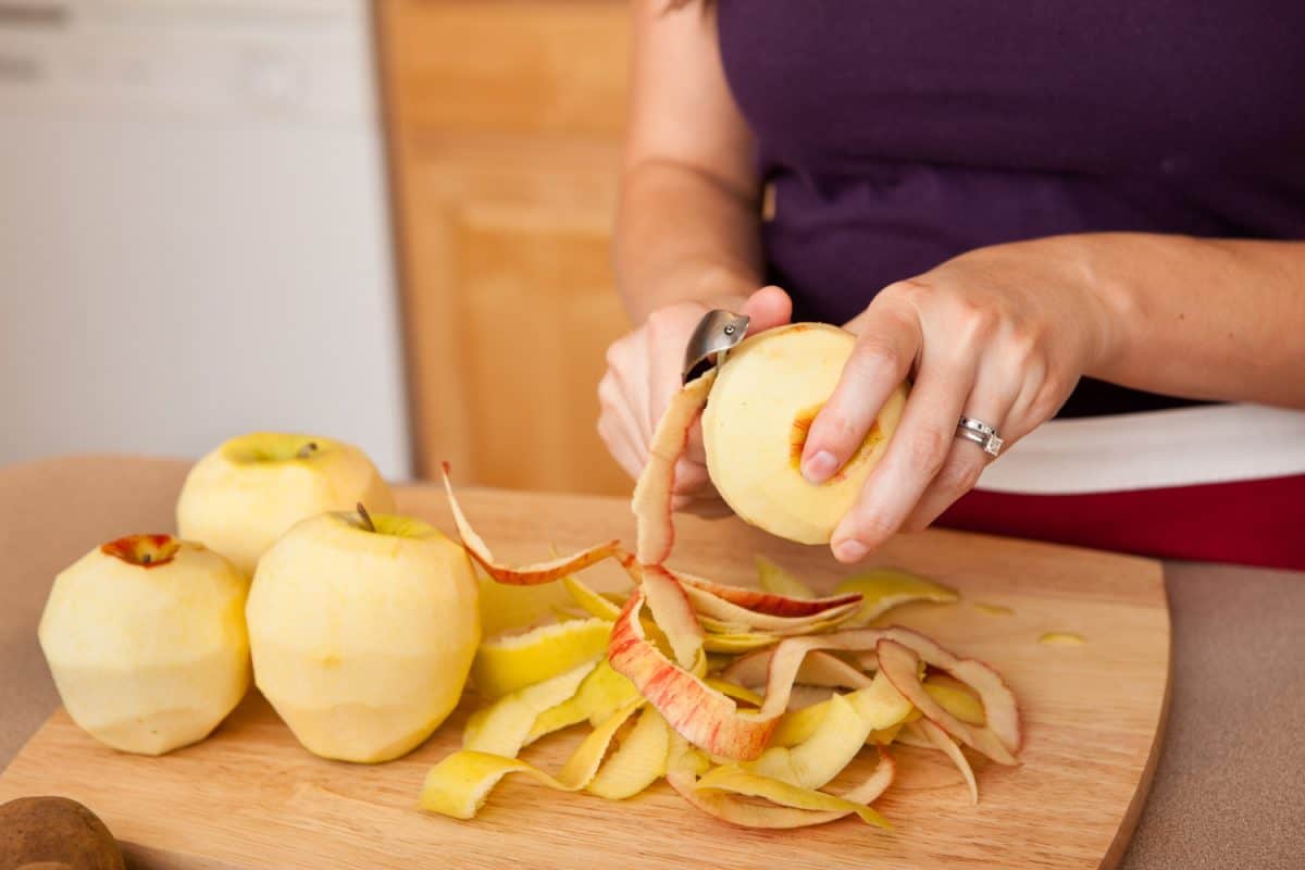 Color photo of a young woman peeling apples in her kitchen at home.
