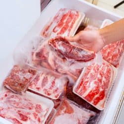 Flat layout of human hand picking a package of red meat, plastic wrapped from the freezer box in the storage room, What Size Chest Freezer For A Whole Cow?