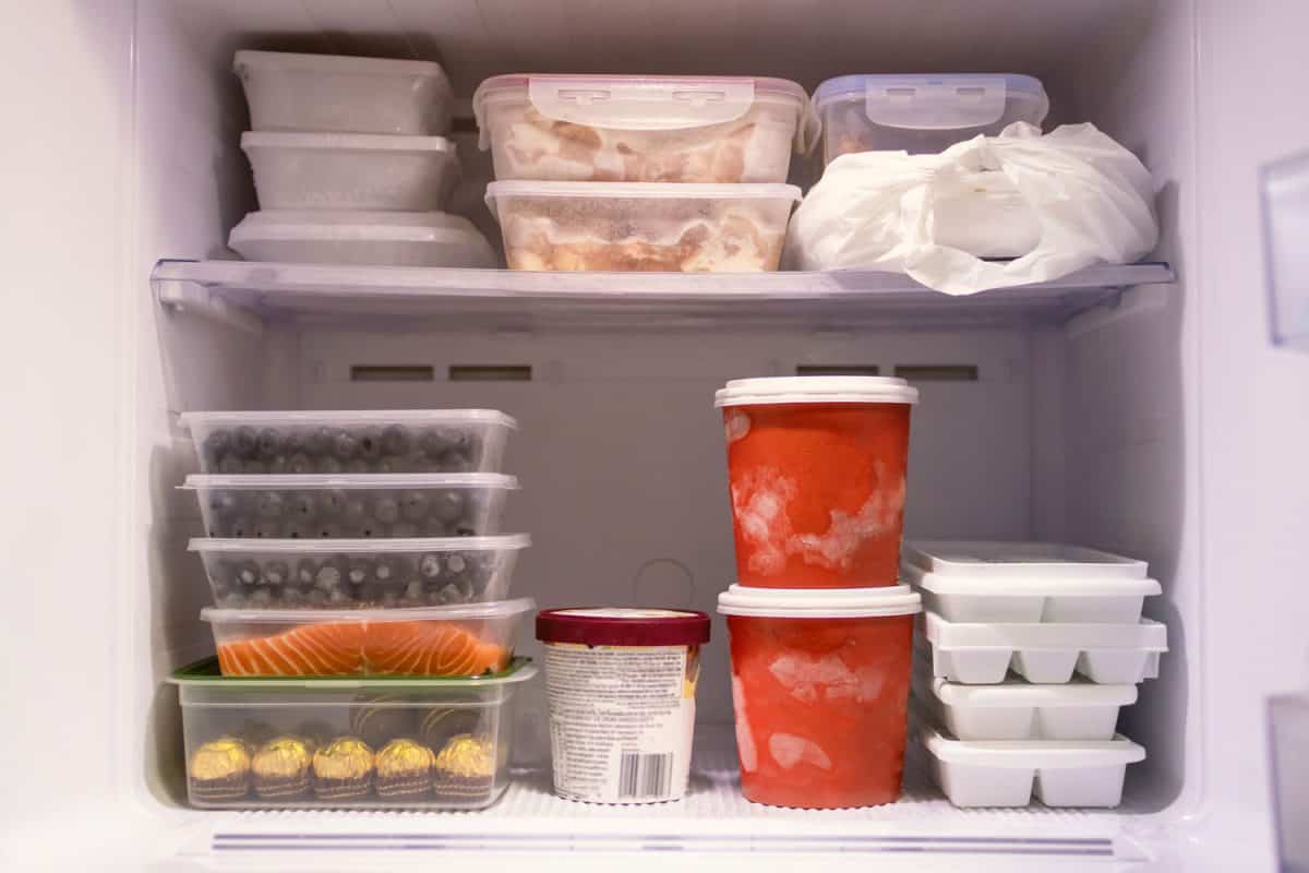 Full of frozen food in refrigerator. Meat, fish, fruit, chocolate, ice, cheese and bucket container ice creams flavors on freezer shelves