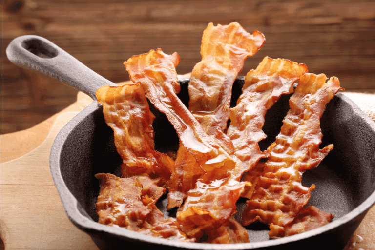 Hot fried bacon pieces in a cast iron skillet. What's The Best Type Of Pan For Cooking Bacon