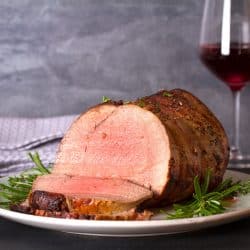 Oven roasted beef served on a white plate garnished with with oregano and wine glasses on the back, Should You Sear A Roast Before Putting It In The Oven?