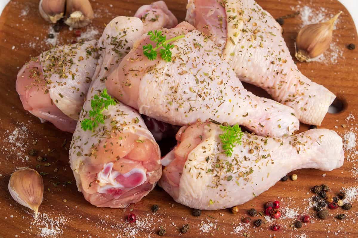 Raw chicken drumstick on a wooden cutting board with spices